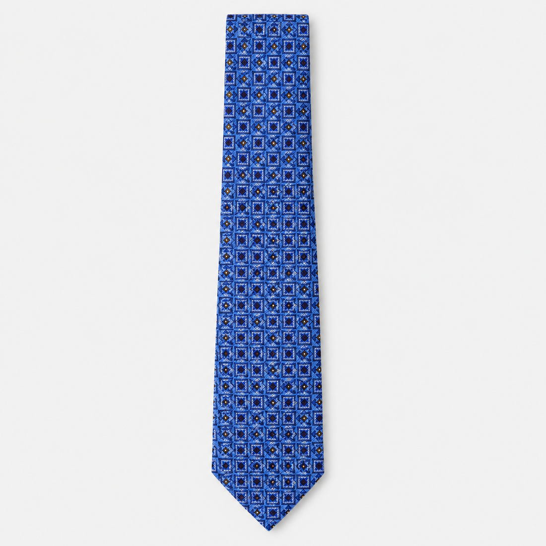 The Catania Tie, a blue silk tie with navy, light blue and gold square motifs on a light grey background.