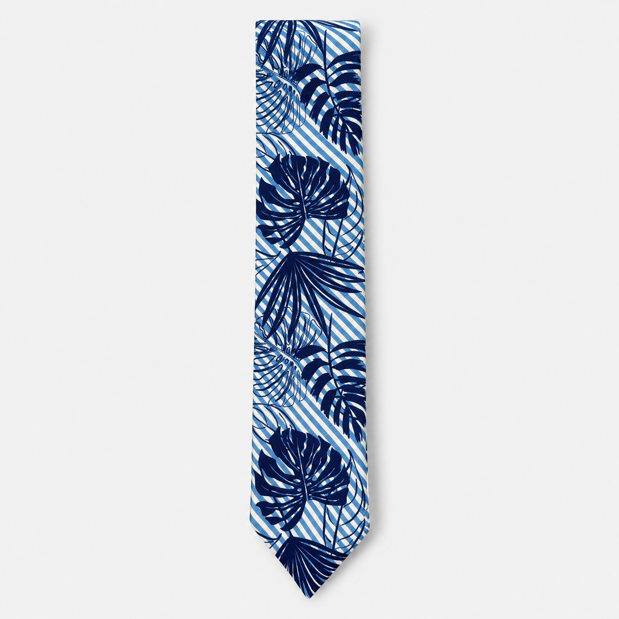 The Taormina Tie, an ivory silk tie with navy tropical leaves and light blue diagonal stripes on a light grey background.