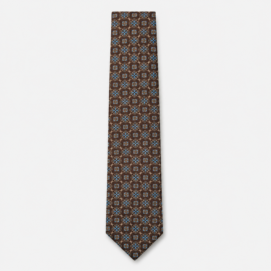 The Udine Tie – rust brown and blue geometric floral silk tie on a light grey background