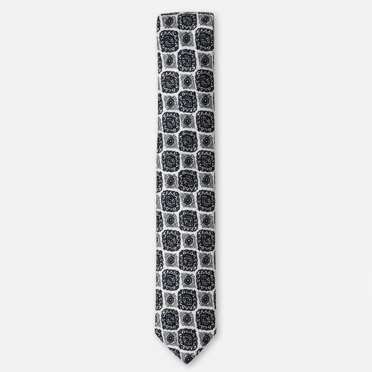 The Avellino Tie – black and ivory square medallion silk tie on a light grey background