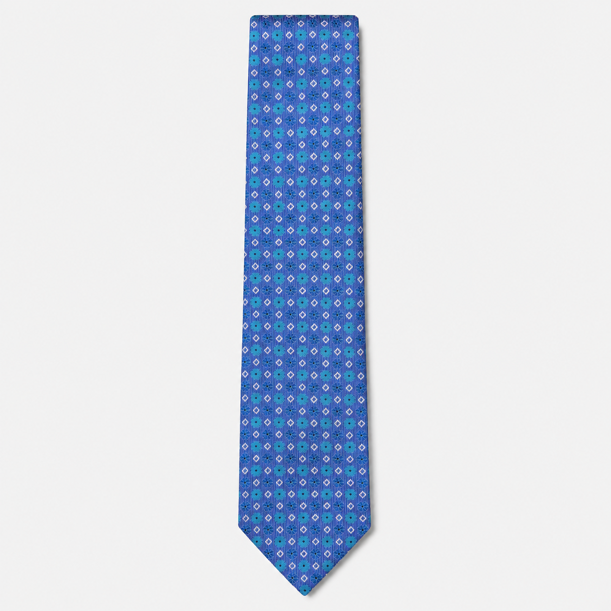 The Ferrara Tie, a royal blue silk tie with turquoise, lavender and white geometric motifs on a light grey background.