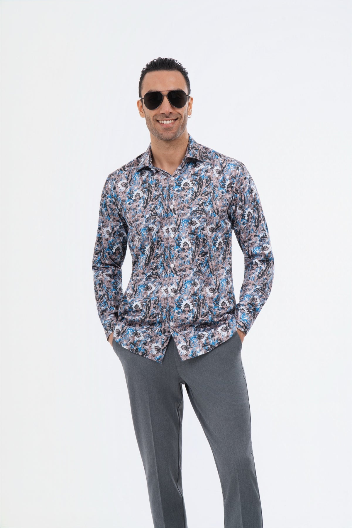 Male model wearing a multicolour paisley shirt with grey trousers in the studio.