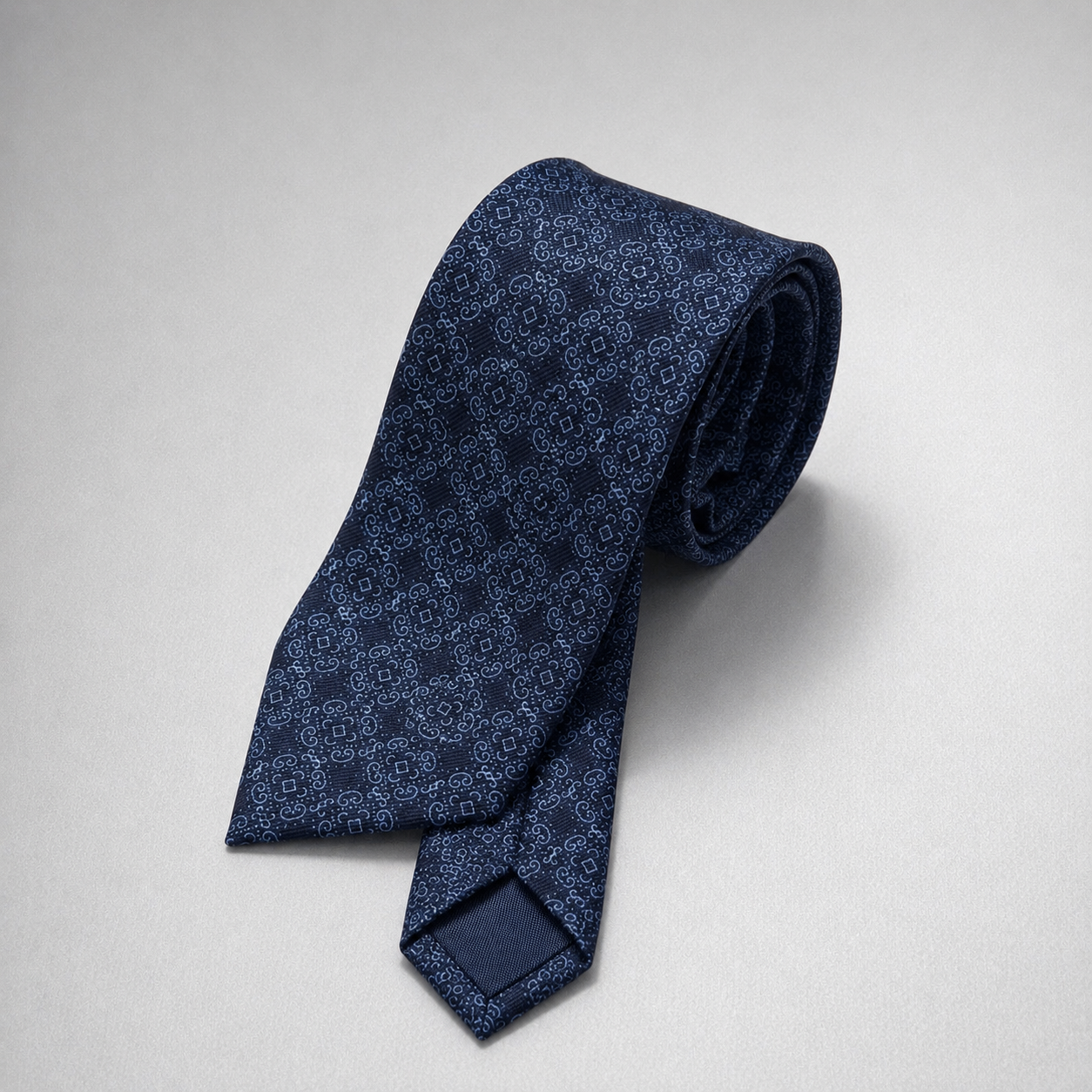Navy tonal floral silk necktie on a grey background.