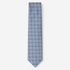 The Positano Tie, a light blue silk tie with white geometric checks and navy accents on a light grey background.