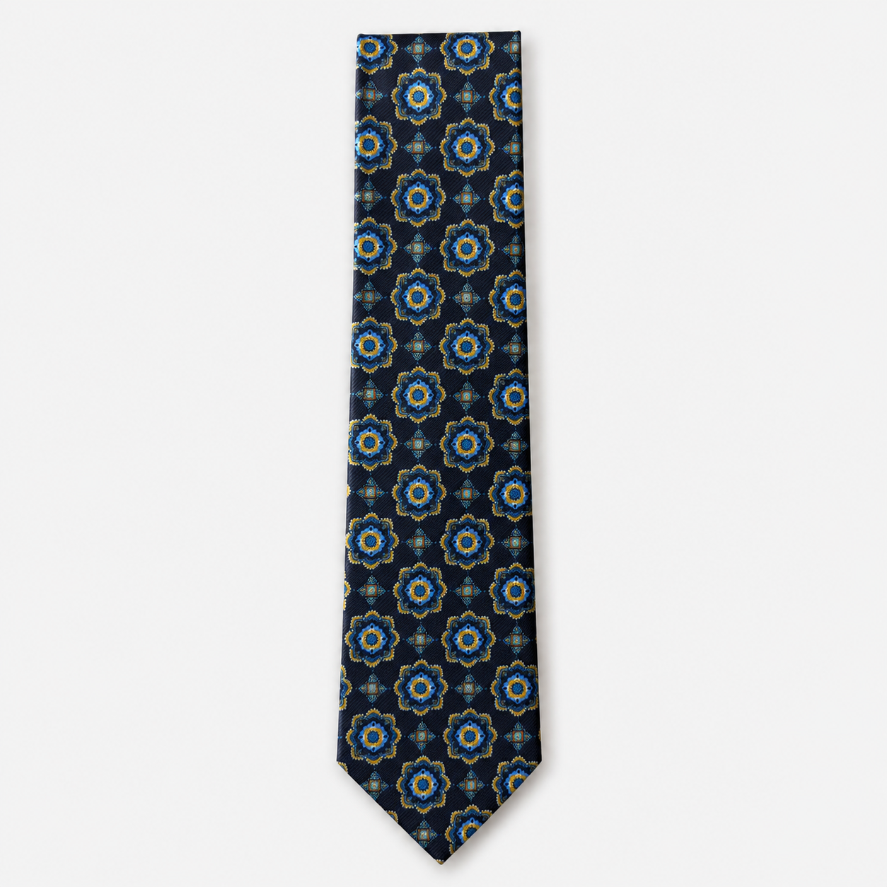 The Savona Tie, a navy silk tie with blue, turquoise and gold rosette medallions on a light grey background.